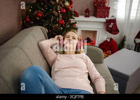 Rilassandosi accanto all'accogliente camino delle vacanze, una giovane donna gode della sua musica preferita mentre abbraccia lo spirito festivo Foto Stock