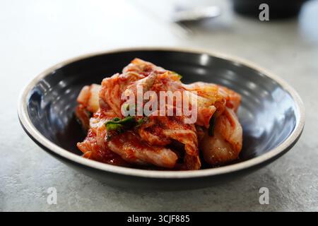 Primo piano del piatto di cavolo fermentato coreano di Kimchi piccante nella ciotola nera Foto Stock