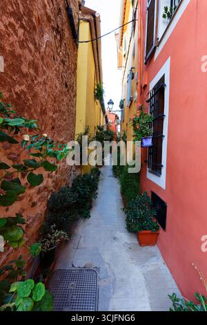 Strada stretta nel centro storico della città francese meridionale di Mentone con case in pietra e facciate colorate Foto Stock