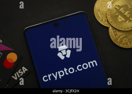 Dhaka, Bangladesh- 26 agosto 2025: Smartphone con logo Crypto.com circondato da monete Bitcoin e carte di pagamento Foto Stock
