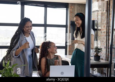 Festeggiando il successo, i colleghi si riuniscono intorno a un notebook in un ufficio moderno, condividendo gioia Foto Stock