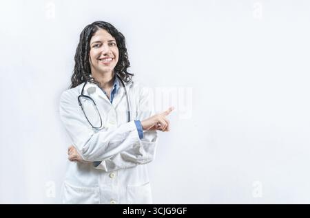 Dottoressa latina che punta da parte isolata. Giovane medico sorridente che punta al lato isolato Foto Stock