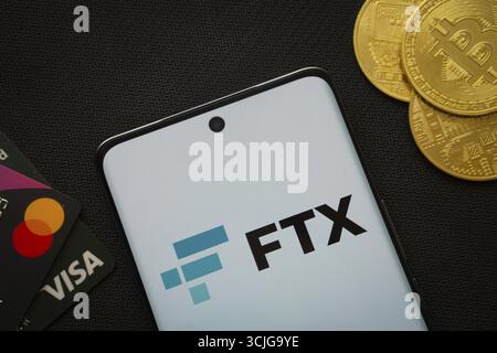 Dhaka, Bangladesh- 26 agosto 2025: Smartphone con logo FTX circondato da monete Bitcoin e carte di pagamento Foto Stock