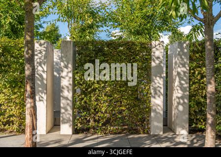 Pareti di cemento e siepi lussureggianti formano una struttura verde all'aperto. Luce e ombra giocano tra le foglie. Foto Stock