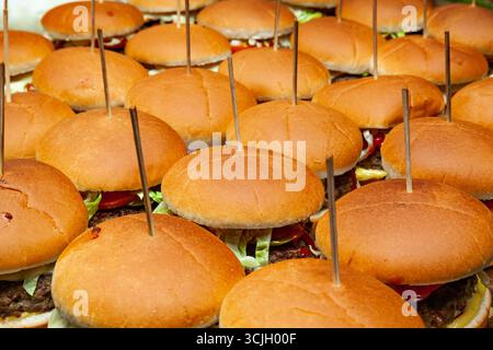 Ci sono molti hamburger con cotolette, formaggio, verdure e bastoncini di legno. Foto Stock