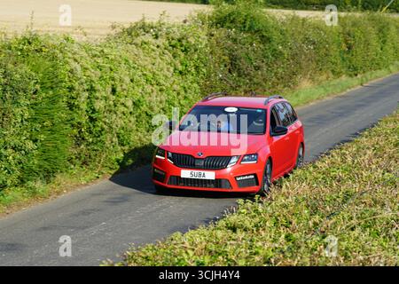 Auto rossa moderna che guida attraverso una strada panoramica di campagna durante il giorno. Shere Hill Climb, East Clandon, Guildford Foto Stock