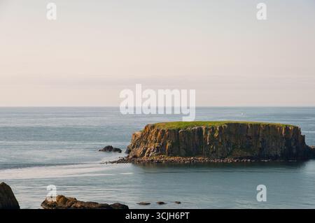 Un'isola rocciosa si trova in mezzo all'oceano. L'acqua è calma e il cielo è limpido Foto Stock