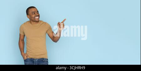 Uomo afroamericano sorridente in camicia casual che punta lateralmente in studio Foto Stock