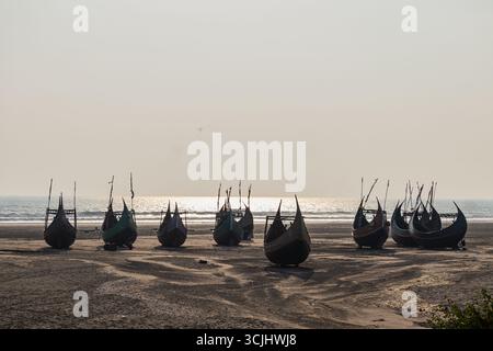 Tradizionali barche da pesca in legno allineate sulla spiaggia sabbiosa all'alba. Foto Stock