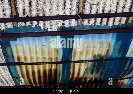 Primo piano astratto di teli ondulati arrugginiti con pannelli blu dipinti e piastrelle di cemento, che mostrano tessuti urbani e decomposizione dei materiali. Foto Stock