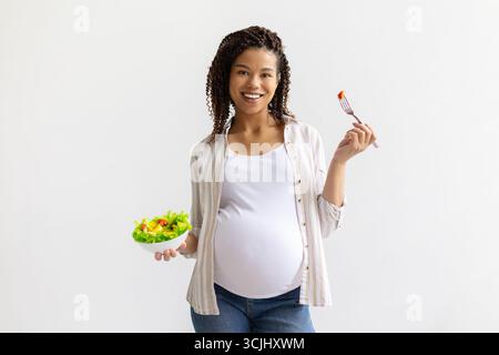 Donna afroamericana sorridente che tiene in mano una ciotola di insalata fresca e forchetta Foto Stock