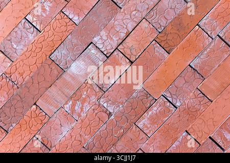 Vista ravvicinata di un motivo a spina di pesce fatto di mattoni rossi. I mattoni sono disposti in diagonale, mostrando la loro consistenza e le loro variazioni di colore Foto Stock
