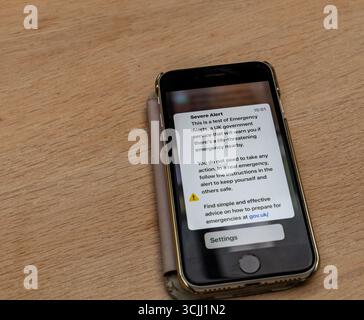 Smartphone che visualizza la notifica di allarme del test di emergenza del governo britannico su una superficie di legno che avverte di una situazione pericolosa per la vita Foto Stock