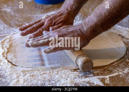 Una base di pizza che viene portata fuori con un mattarello, con una messa a fuoco selettiva Foto Stock