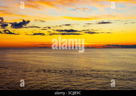 Tramonto sull'oceano dorato con colori vivaci del cielo. Tranquillo paesaggio marino al tramonto con un cielo dorato scintillante, onde dolci e nuvole sparse che creano un Foto Stock