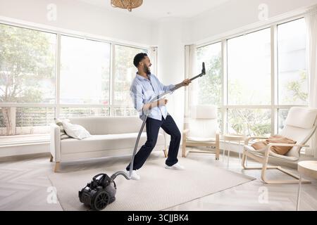 Allegro e energico gen z man che usa l'aspirapolvere come chitarra Foto Stock