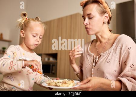 Una madre e sua figlia condividono un momento tranquillo mentre si gusta un pasto insieme nella loro accogliente cucina. La calda atmosfera mette in risalto il loro legame e la loro gioia Foto Stock