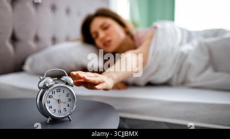 Giovane donna che si sveglia e si spegne sveglia, sdraiata a letto al mattino, non disposta ad andare al lavoro, copia spazio Foto Stock
