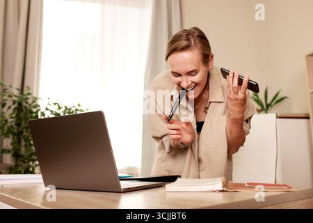Una donna sta svolgendo più attività nel suo spazio di lavoro, gestendo in modo efficiente le chiamate e annotando le informazioni su un notebook, suggerendo la produttività A. Foto Stock