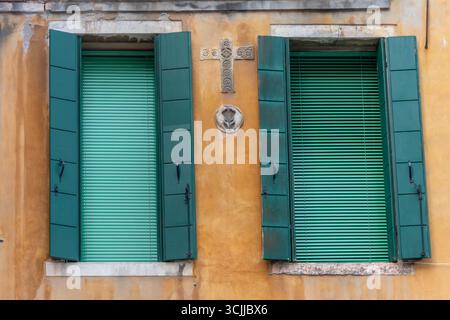 Persiane verdi su una parete gialla con croce decorativa Foto Stock