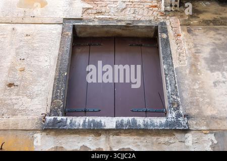 Una vecchia finestra con persiane in legno chiuse su una parete fatiscente Foto Stock