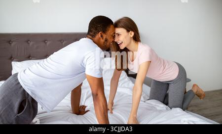 Bella coppia multirazziale divertirsi a letto a casa, toccando le fronte, guardarsi l'un l'altro con amore Foto Stock