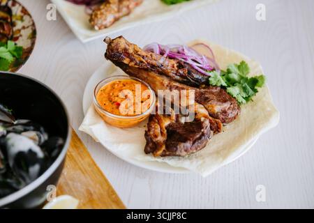 Costolette di agnello grigliate con cipolla rossa, erbe aromatiche e salsa piccante su focaccia di lavanda Foto Stock