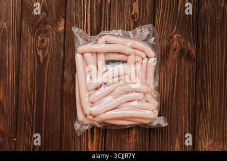 Salsicce di pollo sottovuoto su un tavolo di legno con pomodori e sale sullo sfondo Foto Stock