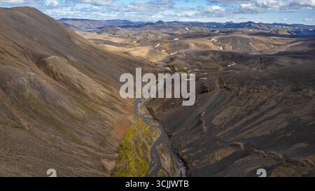 Vista aerea della valle vulcanica in Islanda con fiume intrecciato che si snoda attraverso montagne aride, terreni rocciosi e lontane vette delle Highland Foto Stock