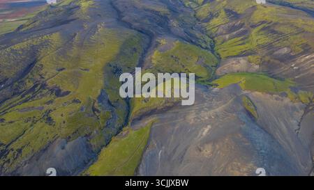 Vista aerea degli altopiani islandesi con pendii vulcanici neri valli coperte di muschio verde e tortuosi fiumi che formano il paesaggio aspro Foto Stock