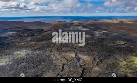 Vista aerea del vasto campo di lava nera in Islanda con crepe e aspre strutture rocciose che si estendono verso il lontano orizzonte oceanico Foto Stock