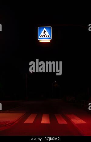 Segnale blu illuminato di attraversamento pedonale di notte a Berlino, Germania Foto Stock