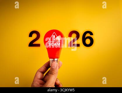 Concetto di allarme truffa 2026 con lampadina di avvertimento rossa e numeri di anno su sfondo giallo. Simbolo della consapevolezza delle frodi online, trucchi truffatori, cybersecu Foto Stock