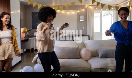 Donne che festeggiano a casa, tengono bevande e sorridono con decorazioni natalizie Foto Stock