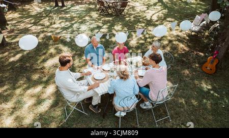 Vista aerea dei nonni, dei genitori e dei bambini che mangiano insieme all'esterno. Foto Stock