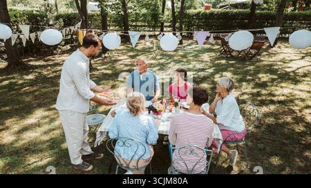 Vista aerea dei nonni, dei genitori e dei bambini che mangiano insieme all'esterno. Foto Stock