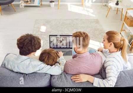 Famiglia, genitori e due figli seduti sul divano, videochiamate online con gli amici tramite laptop. Foto Stock