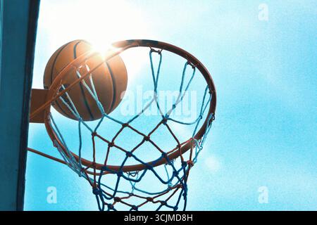 Pallacanestro in canestro, all'aperto con il cielo come sfondo, bordo dorato, sfondo bokeh, simboleggia la vittoria, il successo, successo nello sport Foto Stock