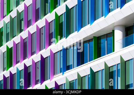 Facciata colorata di un edificio di uffici con pannelli di finestre angolati in una disposizione geometrica verde, viola e blu. Foto Stock