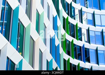 Facciata colorata di un edificio di uffici con pannelli di finestre angolati in una disposizione geometrica verde, viola e blu. Foto Stock