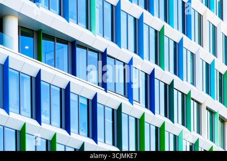 Facciata colorata di un edificio di uffici con pannelli di finestre angolati in una disposizione geometrica verde, viola e blu. Foto Stock