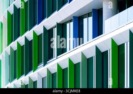 Facciata colorata di un edificio di uffici con pannelli di finestre angolati in una disposizione geometrica verde, viola e blu. Foto Stock