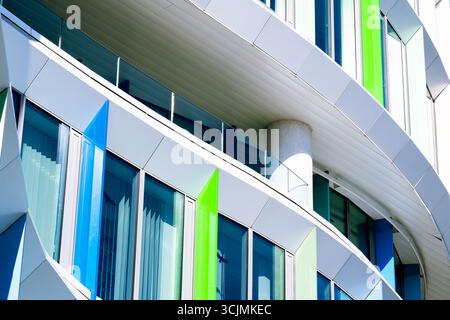 Facciata colorata di un edificio di uffici con pannelli di finestre angolati in una disposizione geometrica verde, viola e blu. Foto Stock