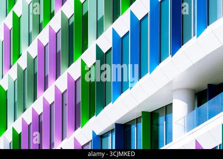 Facciata colorata di un edificio di uffici con pannelli di finestre angolati in una disposizione geometrica verde, viola e blu. Foto Stock