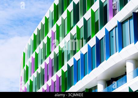 Facciata colorata di un edificio di uffici con pannelli di finestre angolati in una disposizione geometrica verde, viola e blu. Foto Stock