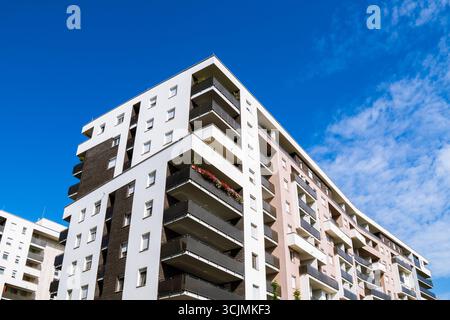 Moderno complesso residenziale con diversi edifici di appartamenti, balconi e design urbano sotto un cielo blu luminoso. Foto Stock