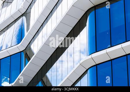 Edificio futuristico per uffici con strutture bianche curve e vetro blu riflettente che creano un design architettonico fluido e moderno. Foto Stock