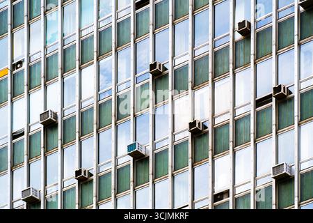 Facciata del vecchio edificio di uffici con finestre ripetitive, pannelli verdi invecchiati e unità di aria condizionata visibili. Foto Stock