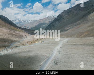 Vista aerea di una strada tortuosa che attraversa il paesaggio arido e aspro verso vette innevate sotto un vasto cielo, Kaza, Himachal Pradesh, India. Foto Stock