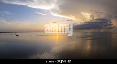 Vista aerea del sole che abbraccia le acque tranquille, dipingendo il cielo con sfumature d'oro e blu, mentre le barche navigano pacificamente all'orizzonte, Key largo, Florida, Stati Uniti. Foto Stock